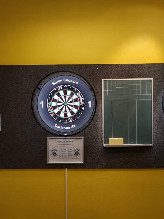 Nærbillede af en oplyst dartskive med kridttavle ved siden af.
