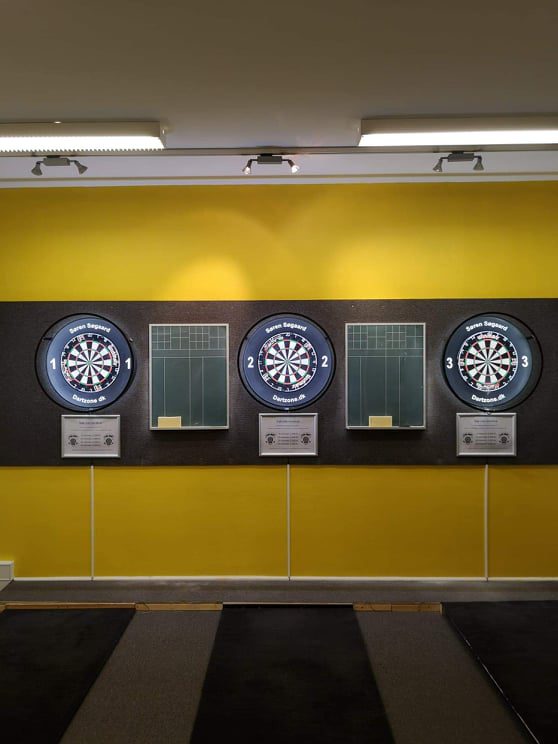 Tre oplyste dartskiver på den gule væg i klublokalet.