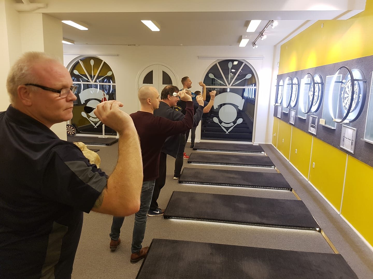 Fem medlemmer står på række ved kastelinjen på en klubaften i Lido Dartklub.